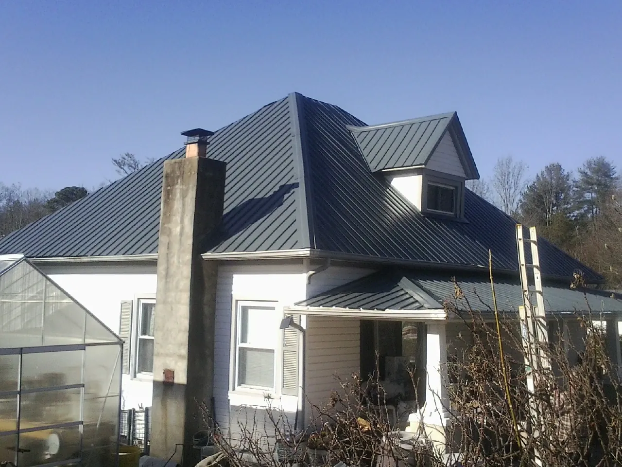 Dark blue standing seam metal roof on a white farmhouse with dormer — Slate & Tile Roof Repair by Roofing Brothers in Eldon