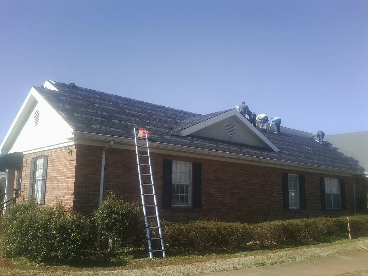 Crew tearing shingles off a brick ranch roof with a ladder set — Emergency Roof Repair work by our crew in Eldon