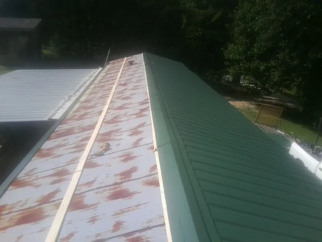 Old rusted panels beside newly installed green metal roofing — Wind Damage Roof Repair by Roofing Brothers in Eldon