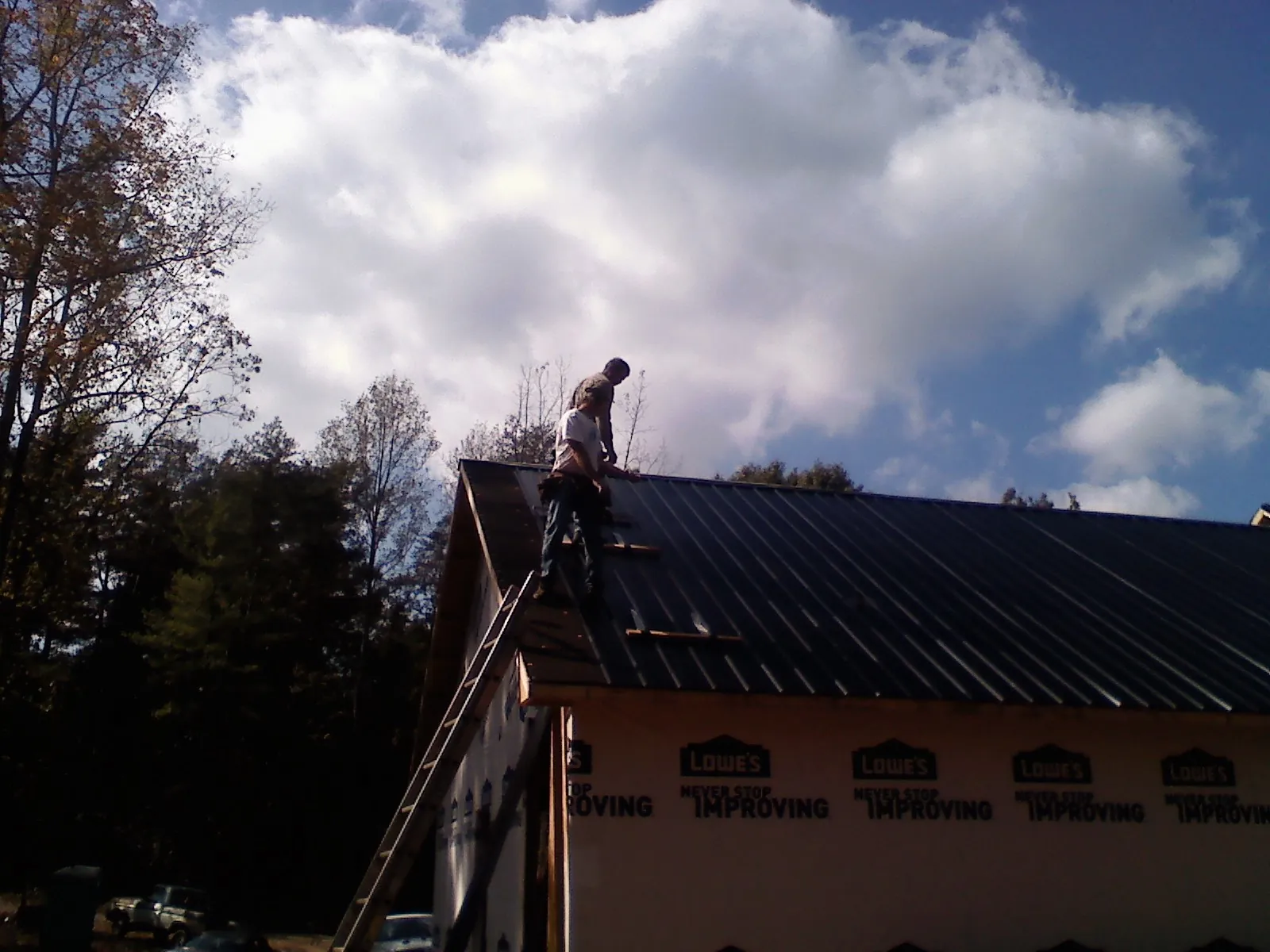 Roofer fastening dark metal panels high against a cloudy sky, from a Roof Inspection job in Eldon